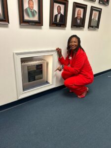 A woman dressed in red kneels in front of a picture-covered wall.